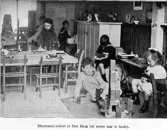 Crianças pequenas trabalham em mesas e no chão em uma sala Montessori de 1915.